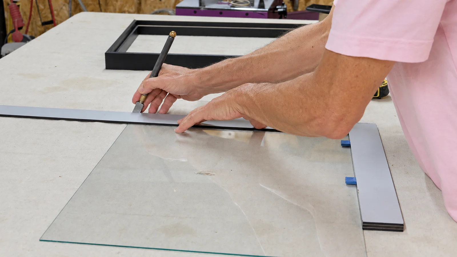 Corte de cristal para enmarcar cuadros con cortavidrios y regla en la mesa del taller.